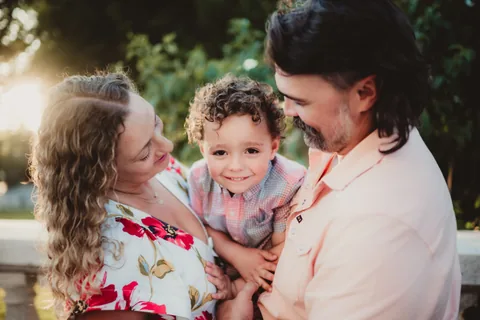 Two adults hold a smiling young child close between them.
