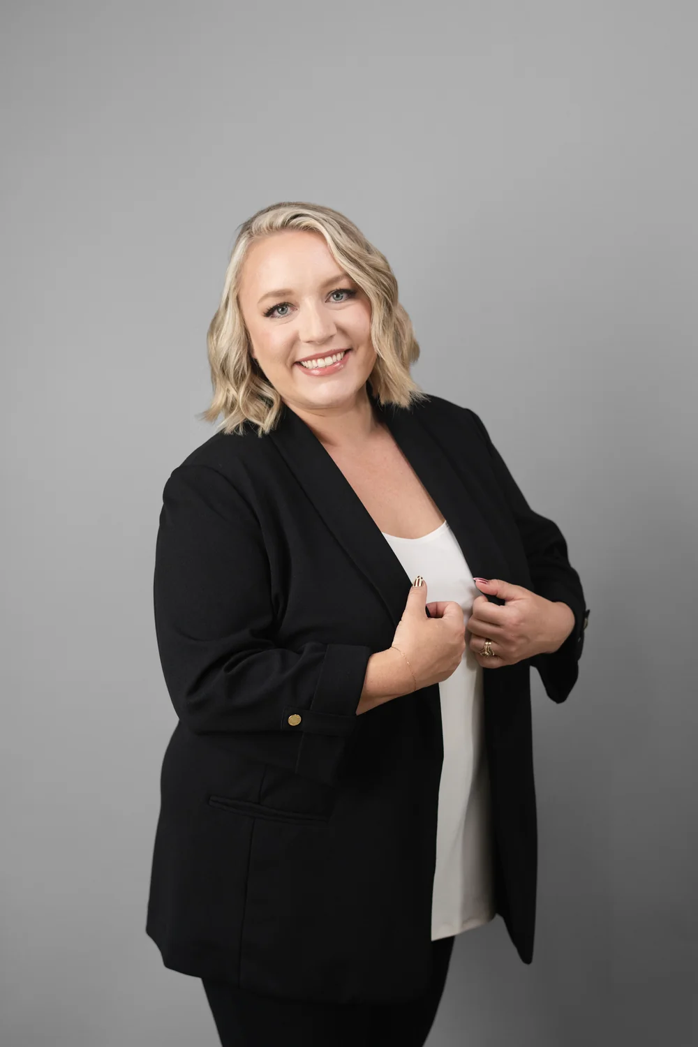 gtw-law-firm-team-headshot-03 Person in a black blazer and white blouse smiling against a gray studio background.