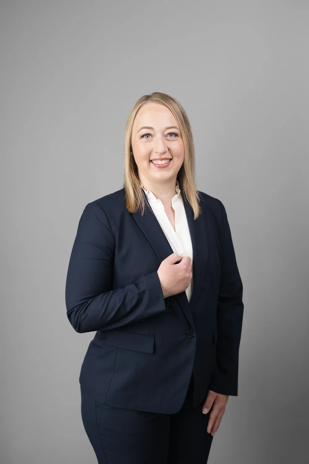 gtw-law-firm-team-headshot-04 Person in a navy blazer and white shirt holding a lapel against a gray studio background.