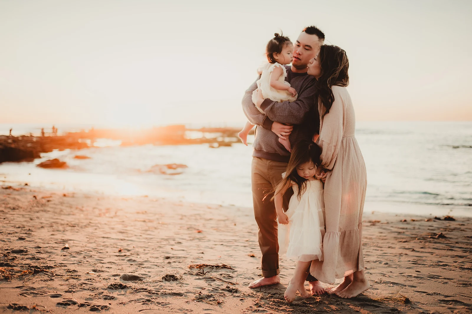 Family embrace by the sea Parents embracing their young child on a beach at sunset.