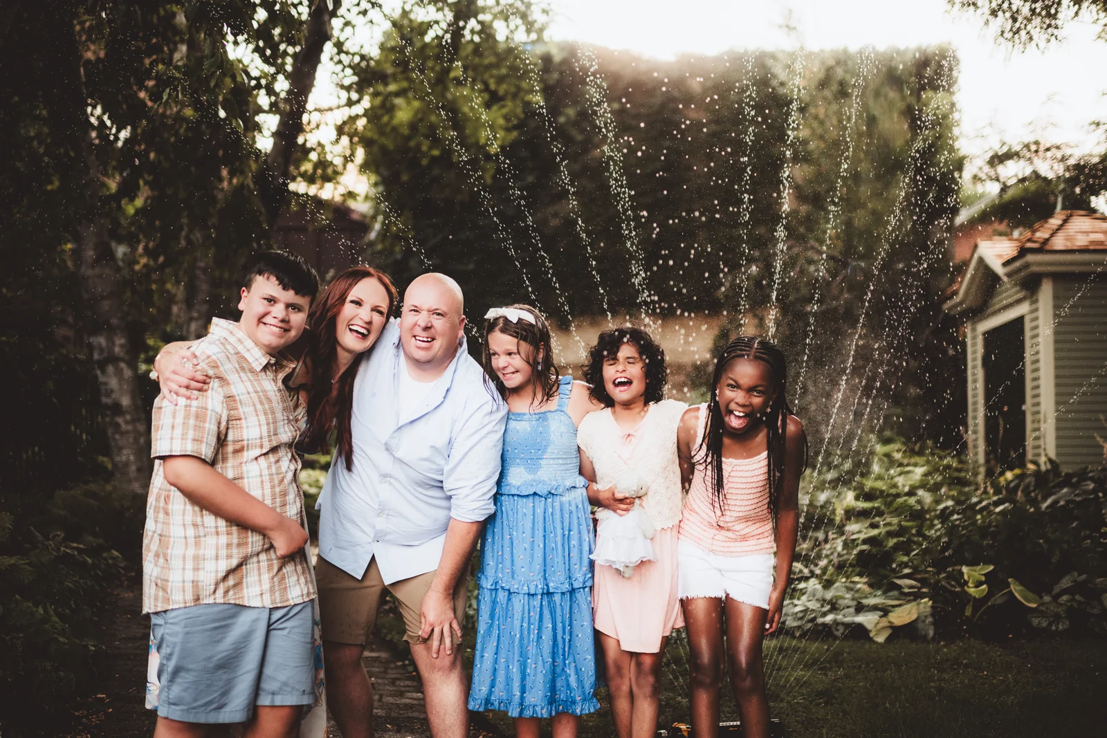 Family garden group portrait A family laughing together as water sprays overhead in a garden.