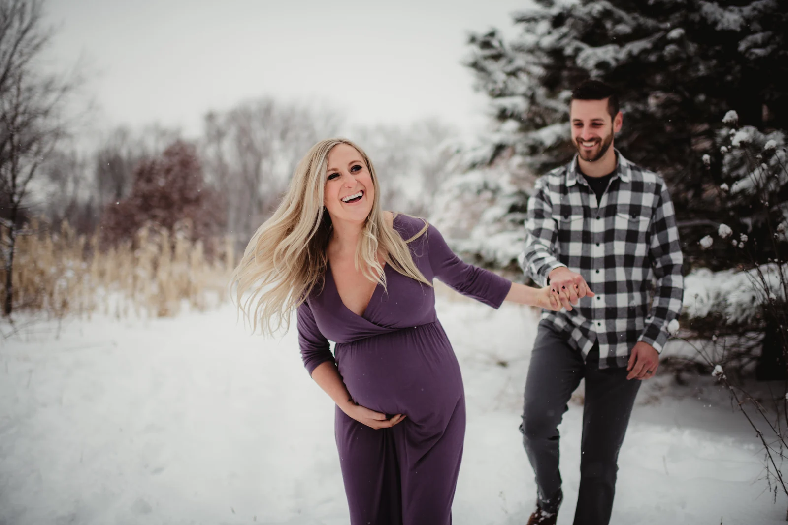 A laughing winter maternity session An expecting couple laughing together in a snowy landscape.