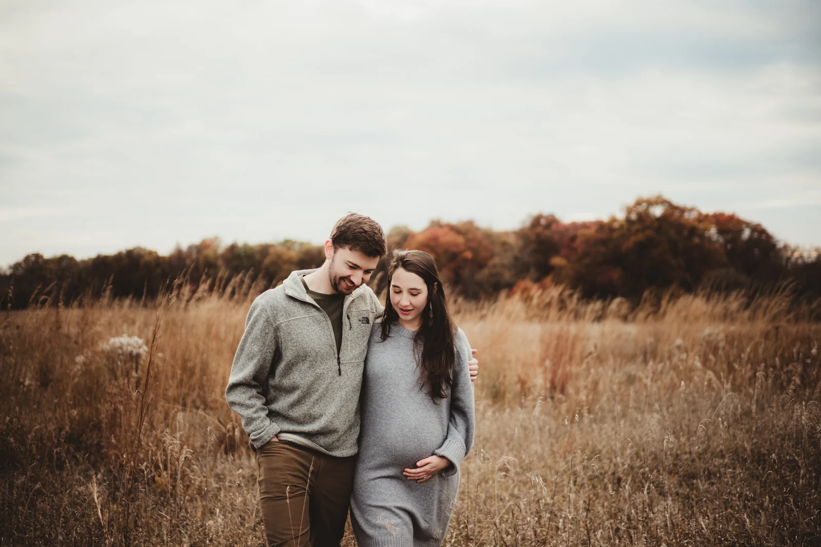 Expecting couple in a grassy field An expecting couple standing close together in a field of tall grass.