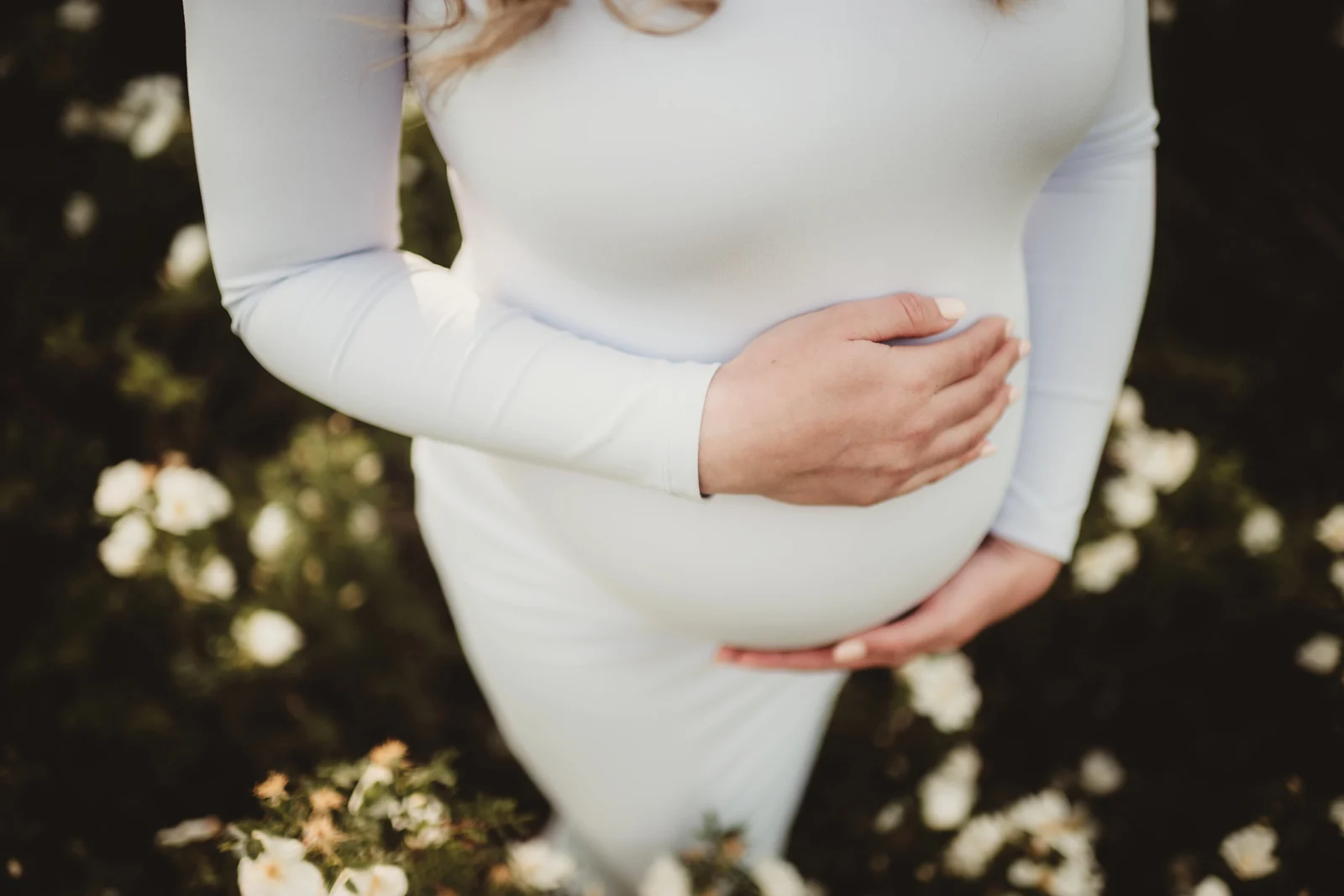 Hands resting on a growing belly A close view of hands resting on a growing belly in a white dress.