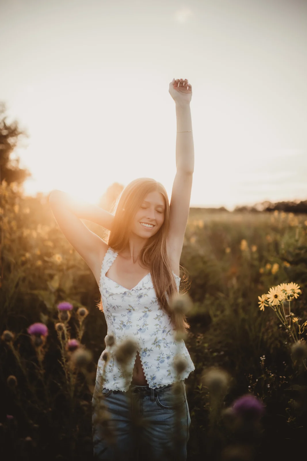 to-senior-2026-senior-celebrating-in-wildflowers A senior raising one arm while standing among sunlit wildflowers.