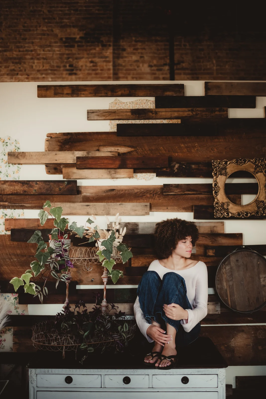 to-senior-2026-senior-creative-studio-portrait A senior seated in a studio with a wood wall and plants.