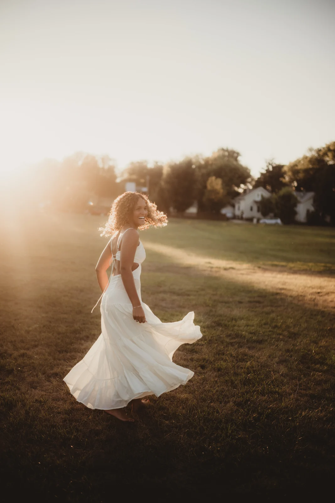 to-senior-2026-senior-dress-in-motion A senior turning in a flowing white dress in a sunlit field.