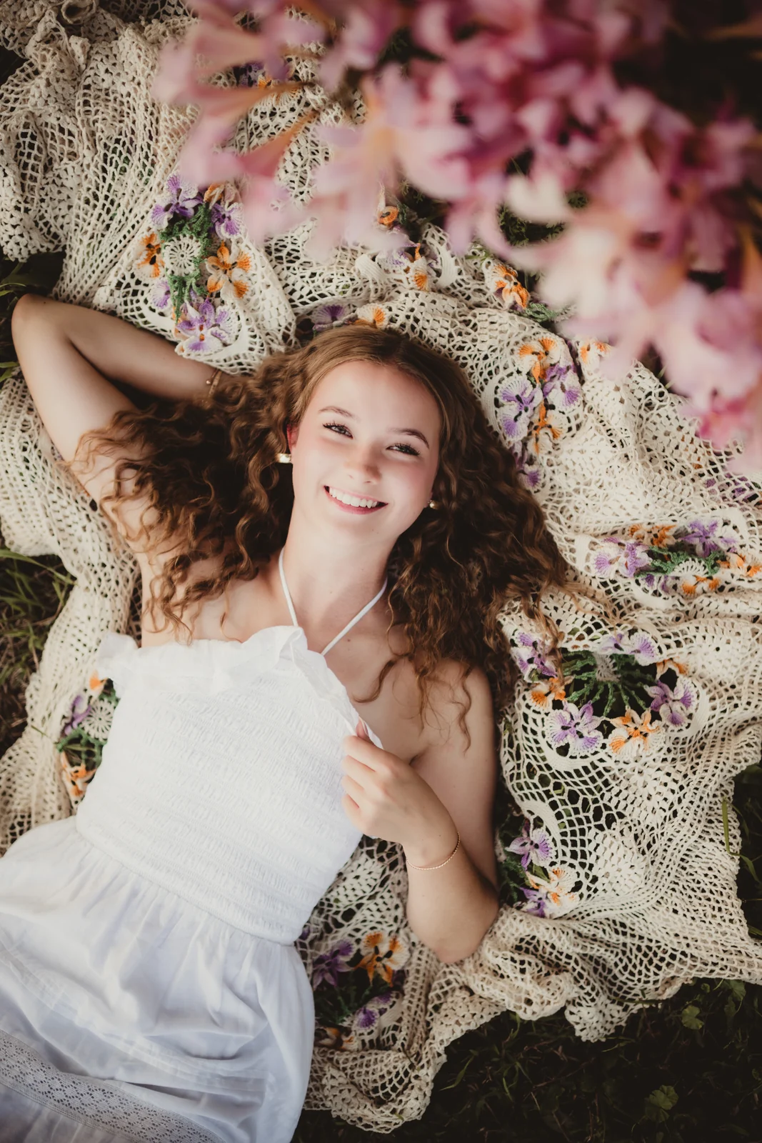 to-senior-2026-senior-flowers-from-above A senior reclining on a patterned blanket surrounded by flowers.