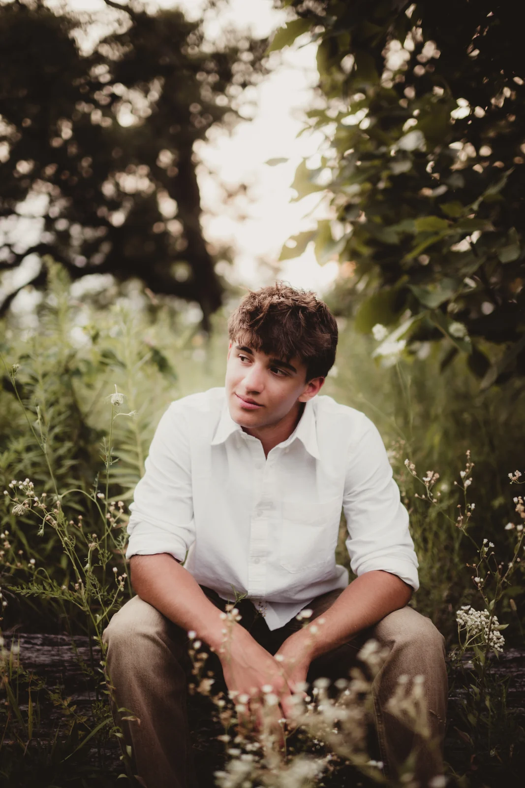 to-senior-2026-senior-garden-portrait A senior in a white shirt seated among leafy plants.
