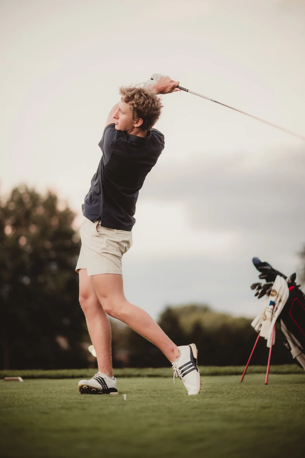to-senior-2026-senior-golf-swing A senior swinging a golf club beside a golf bag outdoors.