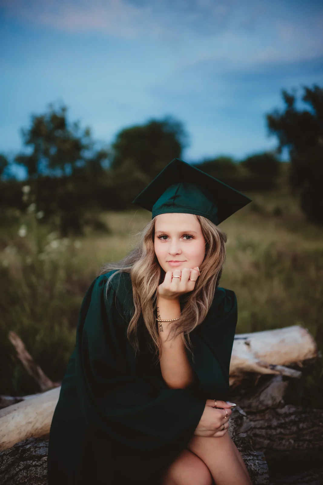 to-senior-2026-senior-graduation-cap A senior in a green graduation cap and gown seated outdoors.