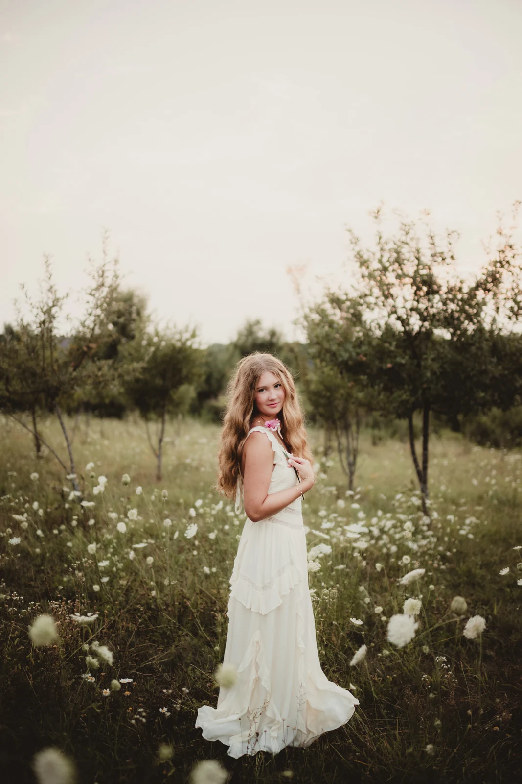 to-senior-2026-senior-in-a-wildflower-meadow A senior in a white dress standing among small white wildflowers.