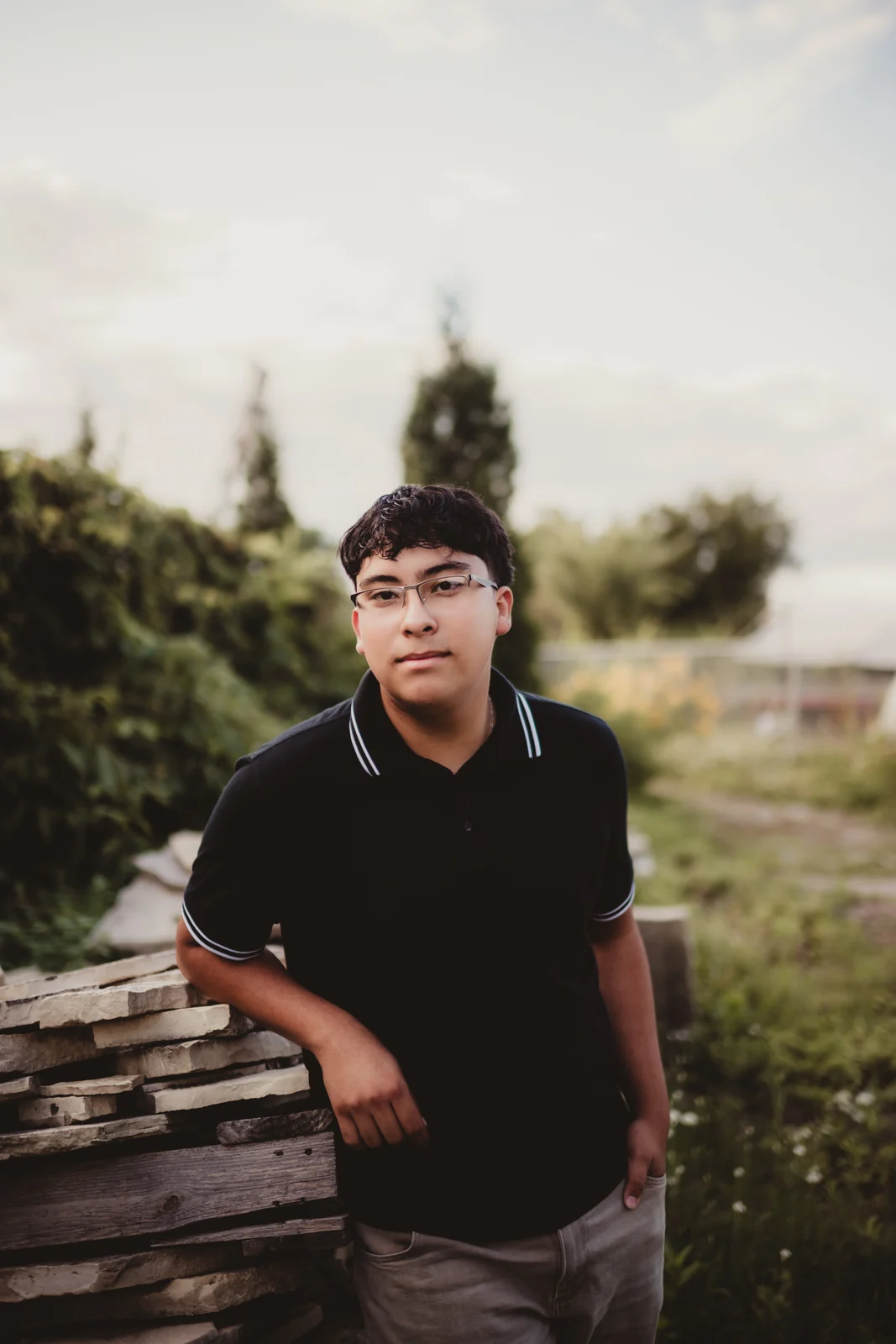 to-senior-2026-senior-industrial-portrait A senior in a black polo shirt standing beside stacked stone.