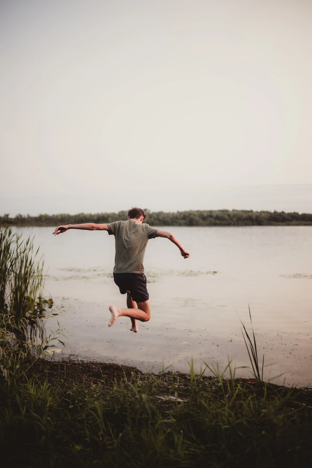 to-senior-2026-senior-jumping-by-the-water A senior jumping beside the water with arms stretched wide.