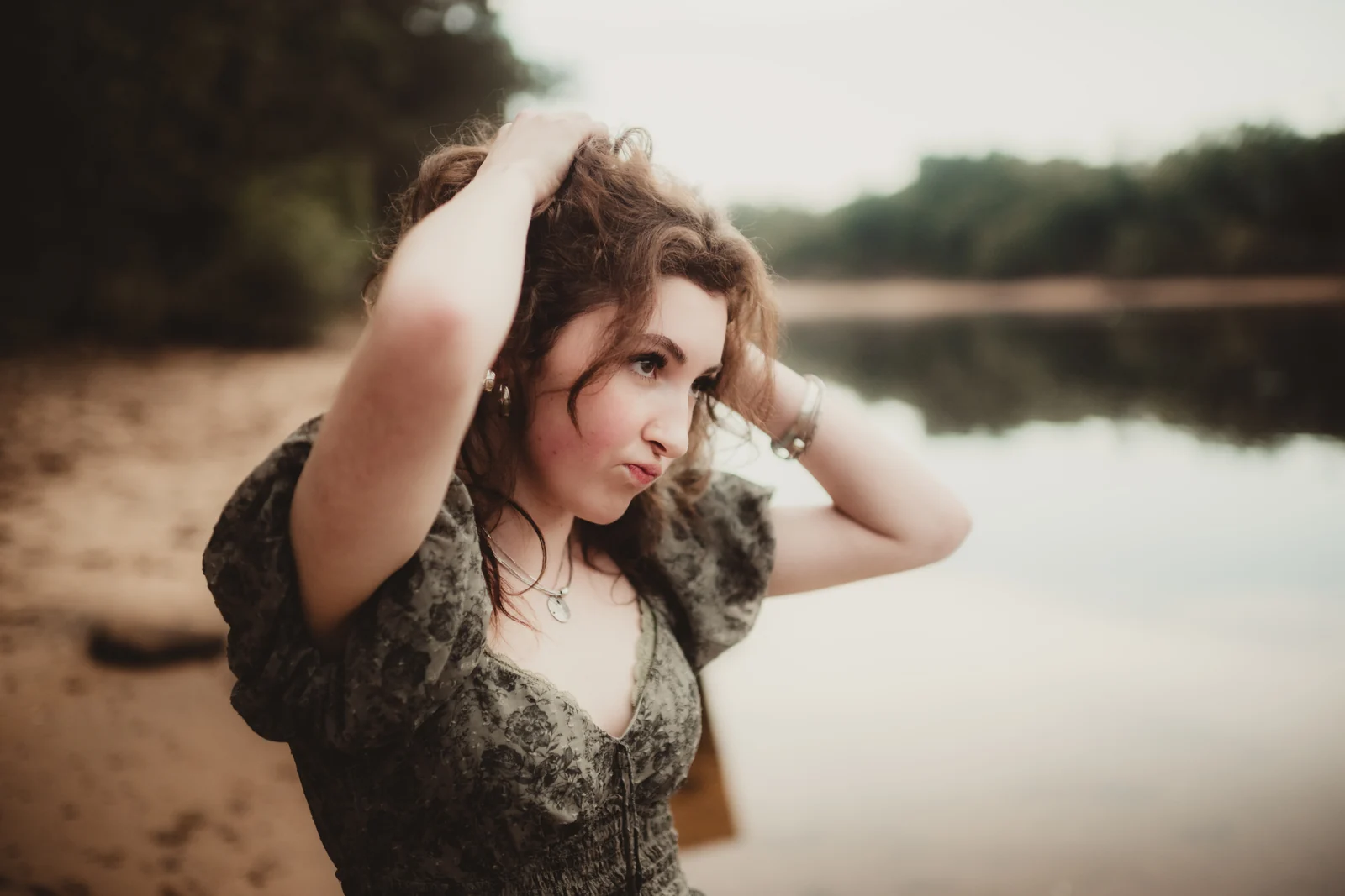to-senior-2026-senior-lakeside-close-up A senior with one hand in her hair beside calm water.