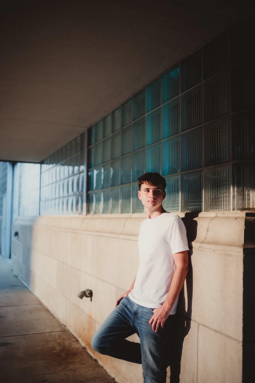 to-senior-2026-senior-modern-building-portrait A senior in a white T-shirt beside blue windows and a concrete wall.