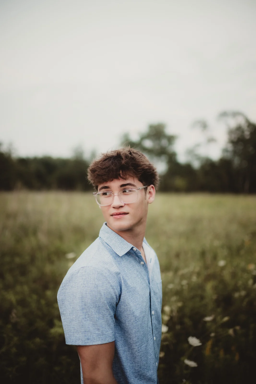 to-senior-2026-senior-open-field-portrait A senior in a light blue shirt standing in an open field.