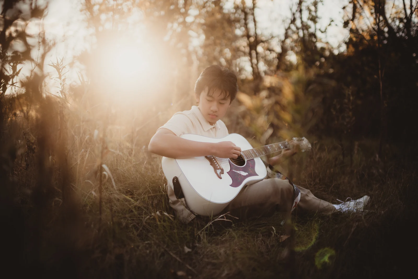 to-senior-2026-senior-playing-guitar A senior playing an acoustic guitar in warm woodland light.