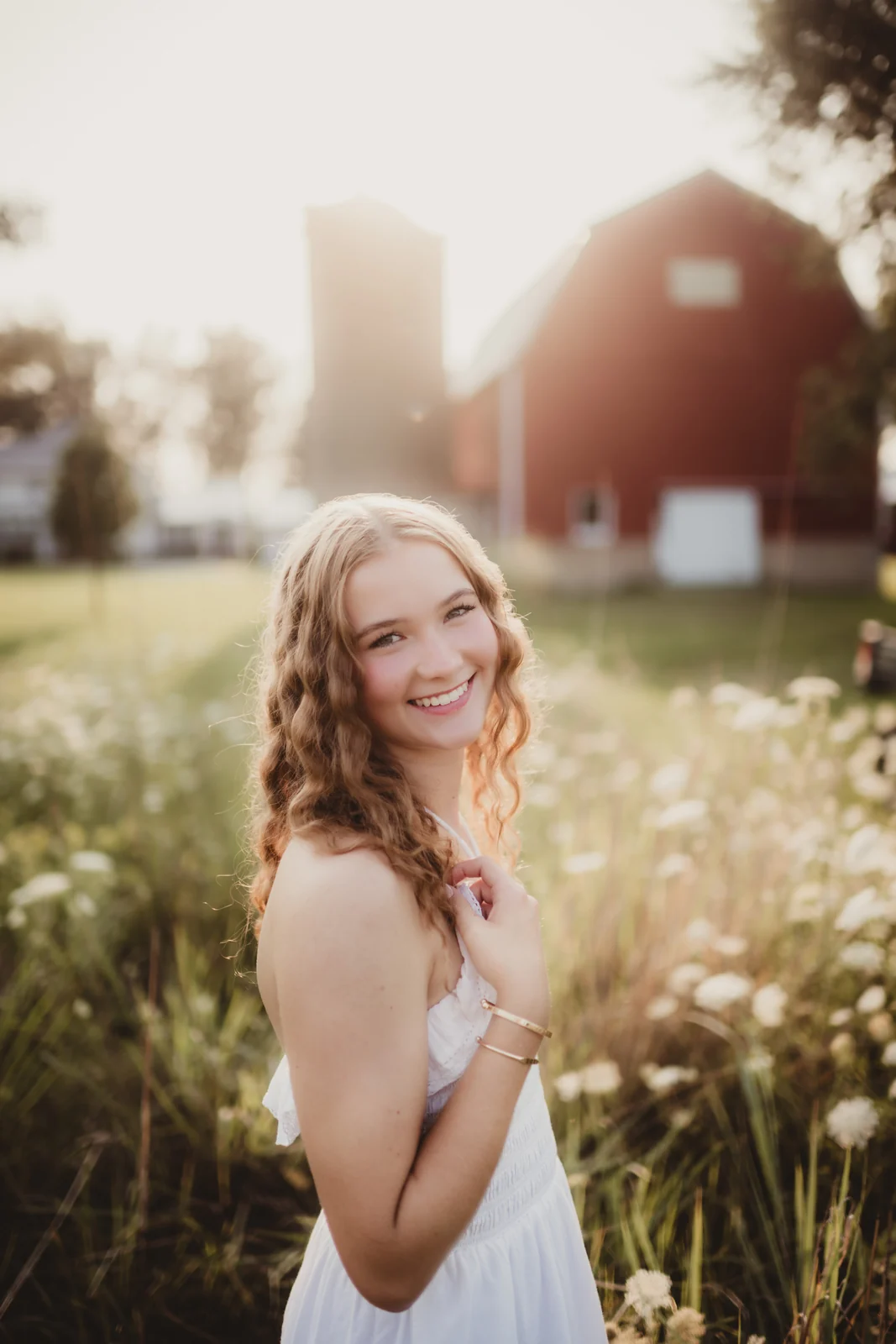 to-senior-2026-senior-red-barn-portrait A senior smiling among wildflowers near a red barn.