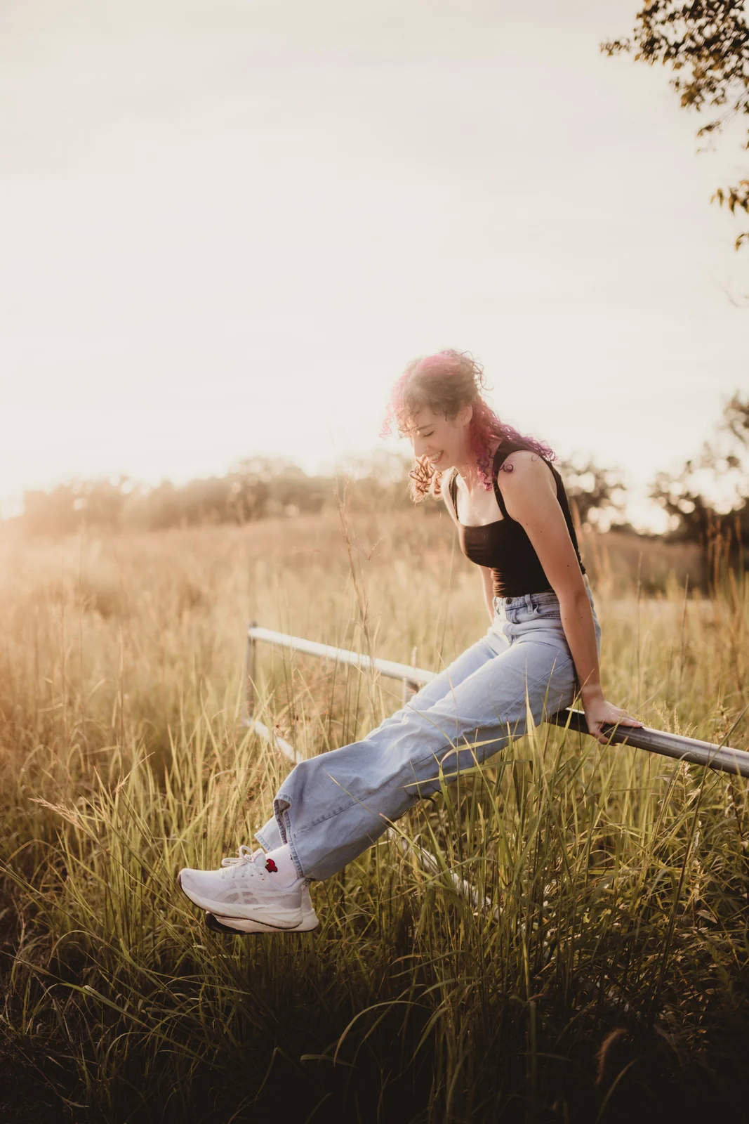 to-senior-2026-senior-seated-in-golden-grass A senior seated on a low rail among golden grasses.