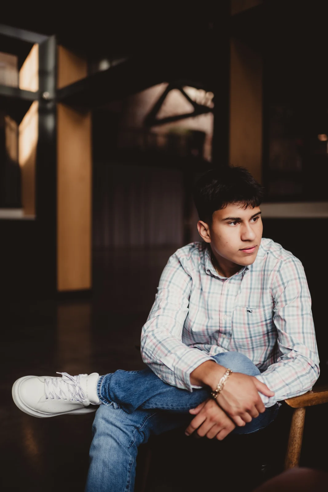 to-senior-2026-senior-seated-studio-portrait A senior in a checked shirt seated on a chair in soft window light.
