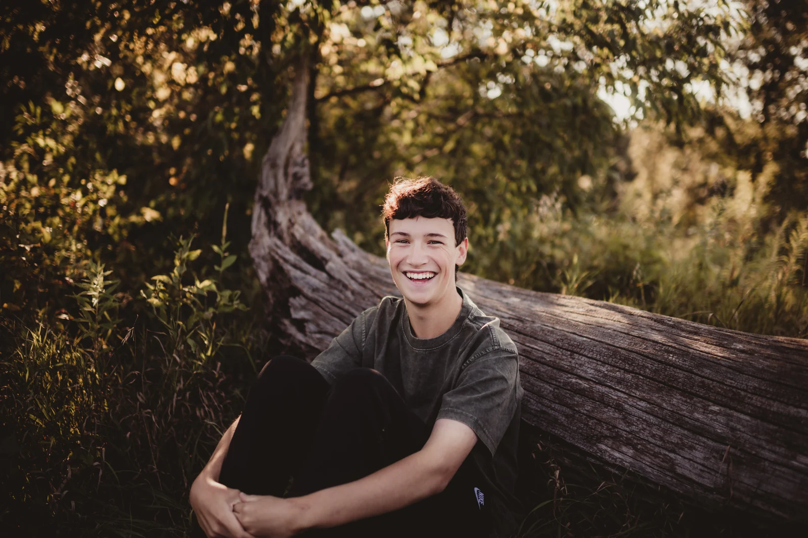 to-senior-2026-senior-smiling-on-fallen-tree A senior smiling while seated on a fallen tree.