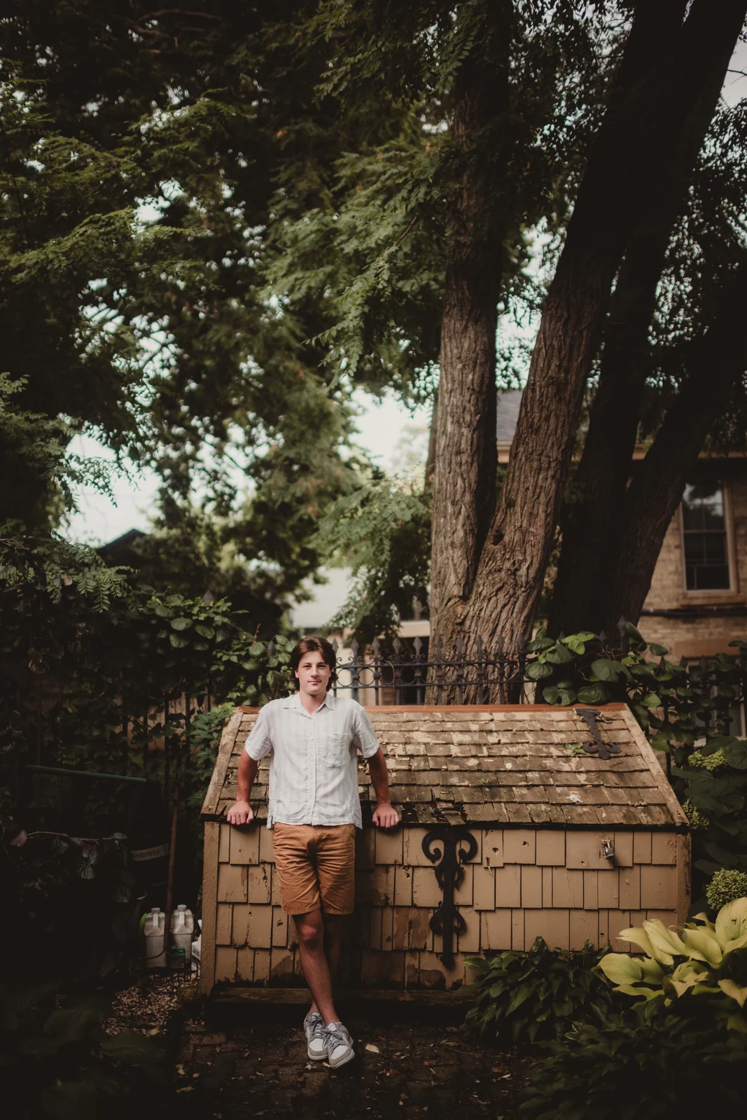 to-senior-2026-senior-tree-lined-street A senior leaning against a low wall on a tree-lined street.
