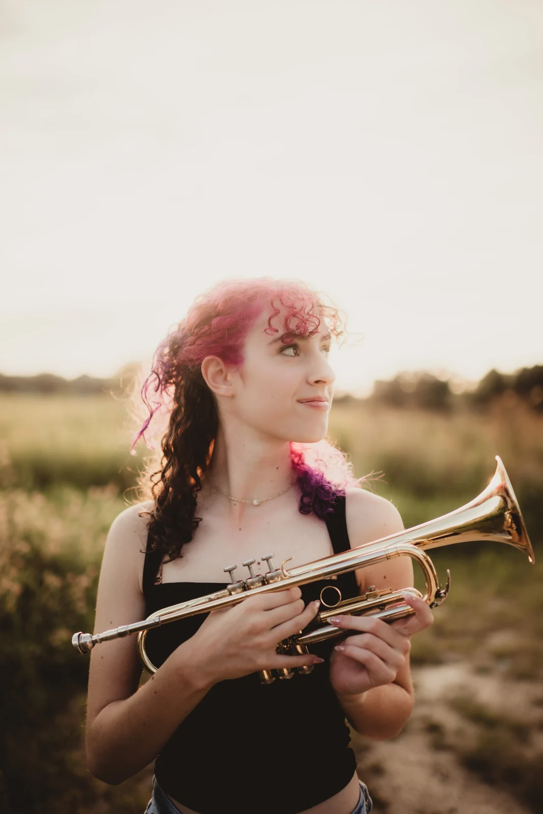 to-senior-2026-senior-with-trumpet A senior with pink hair holding a trumpet in an open field.