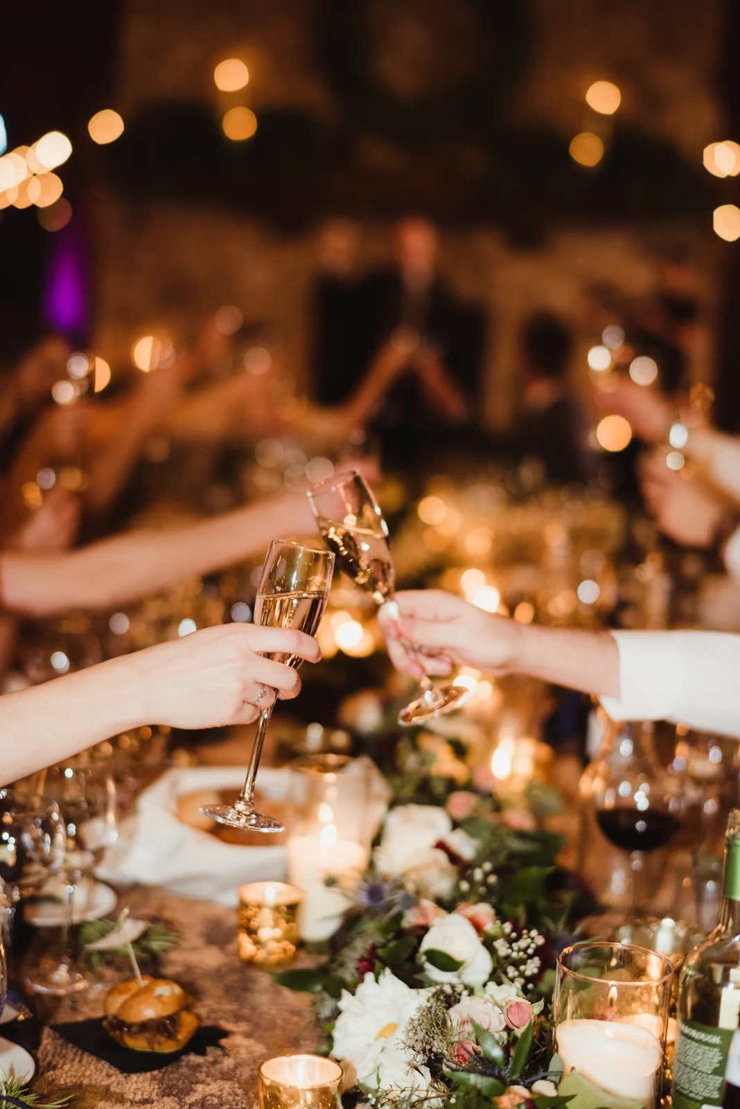 Wedding table in candlelight Guests raising glasses in a toast over a flower-filled wedding reception table.