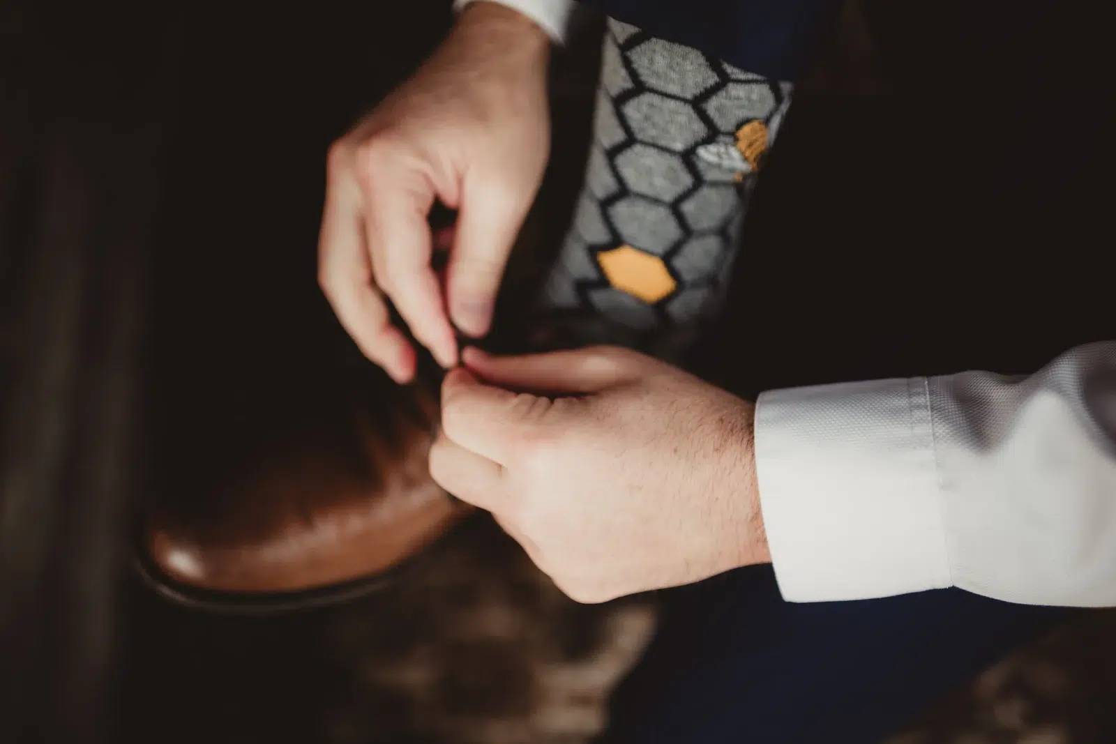 Close-up of hands tying a brown leather shoe below a honeycomb-patterned sock.