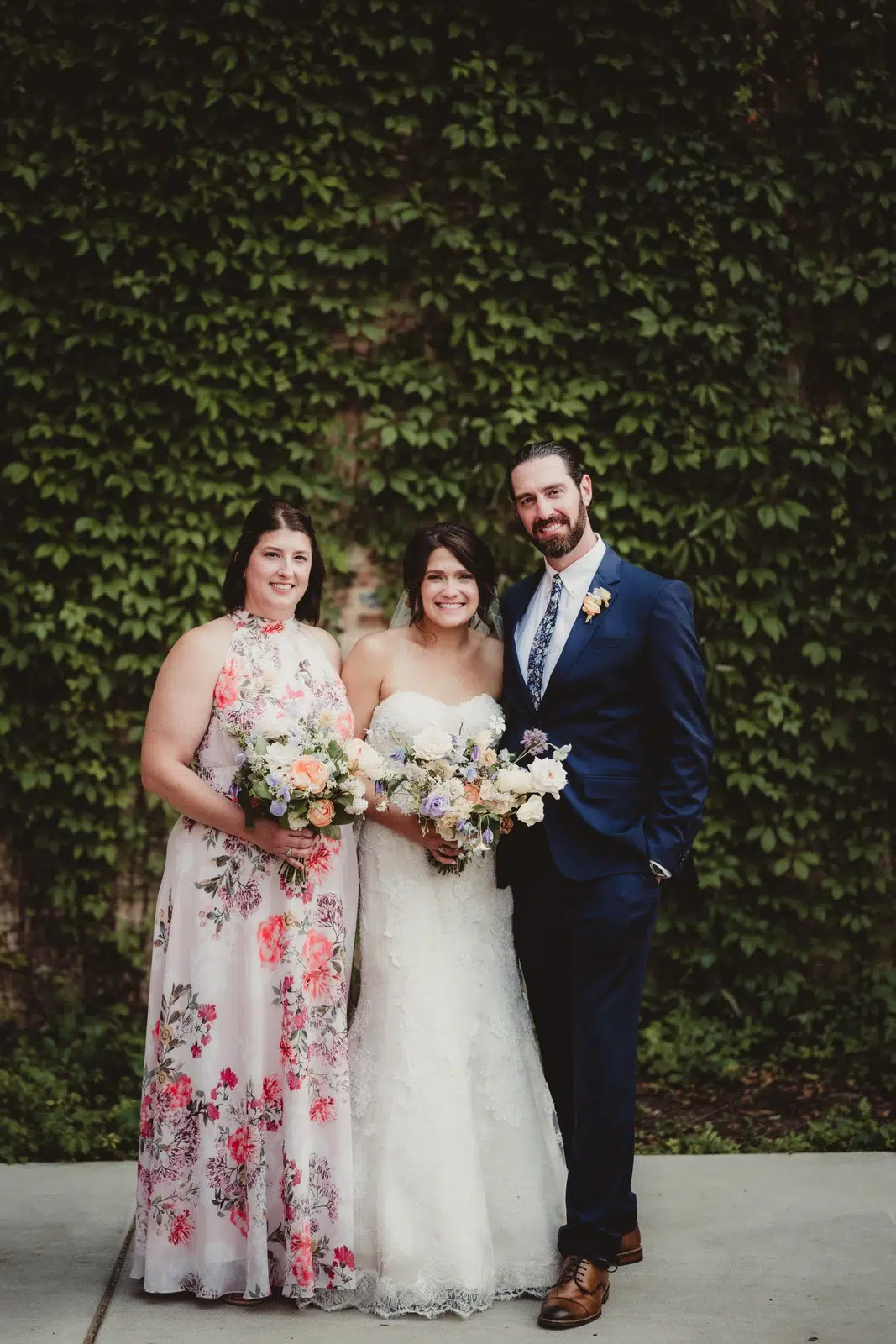 Bride posing between a woman in a floral dress and a man in a blue suit.