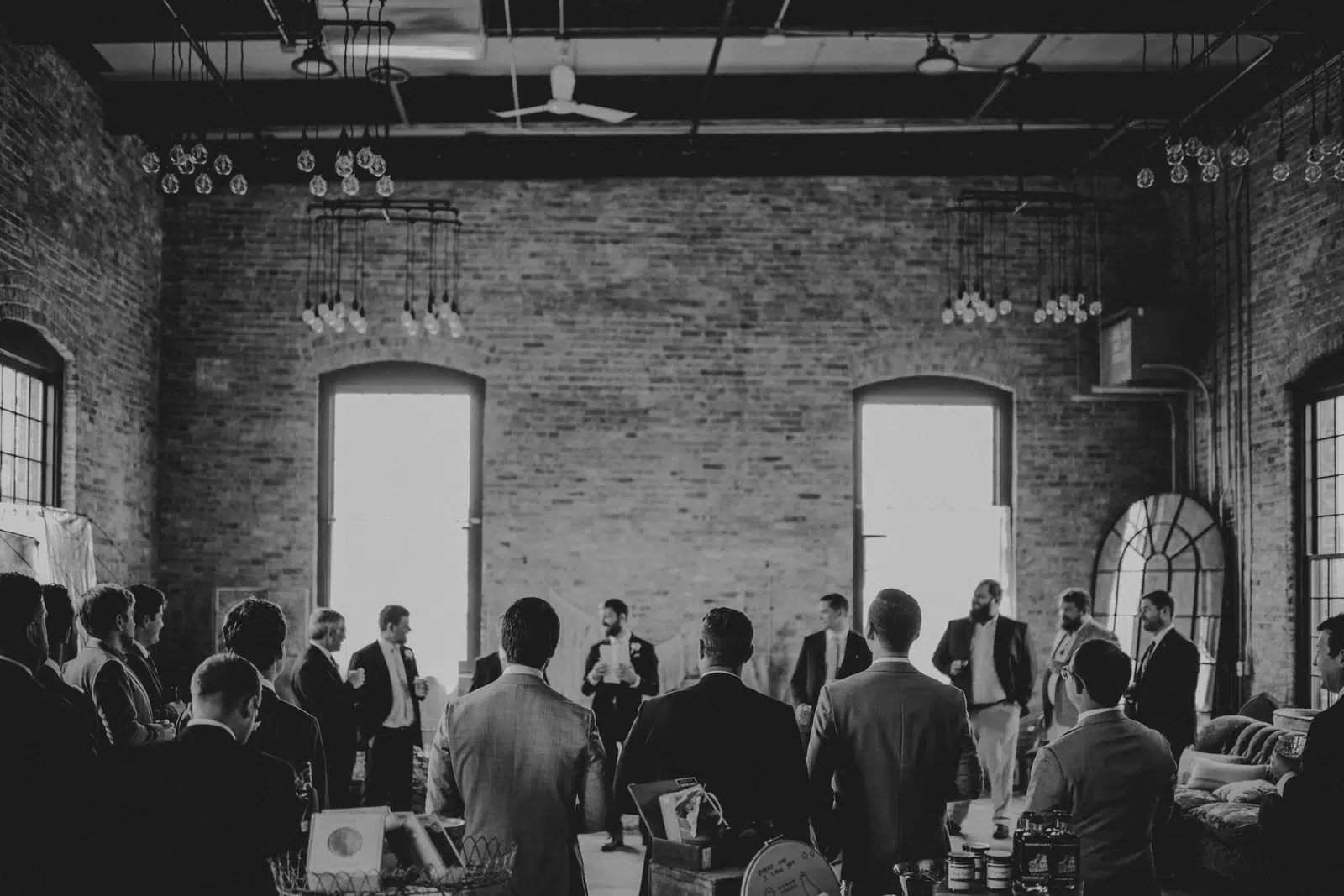 Black-and-white view of guests gathered beneath tall windows and exposed ceiling beams.
