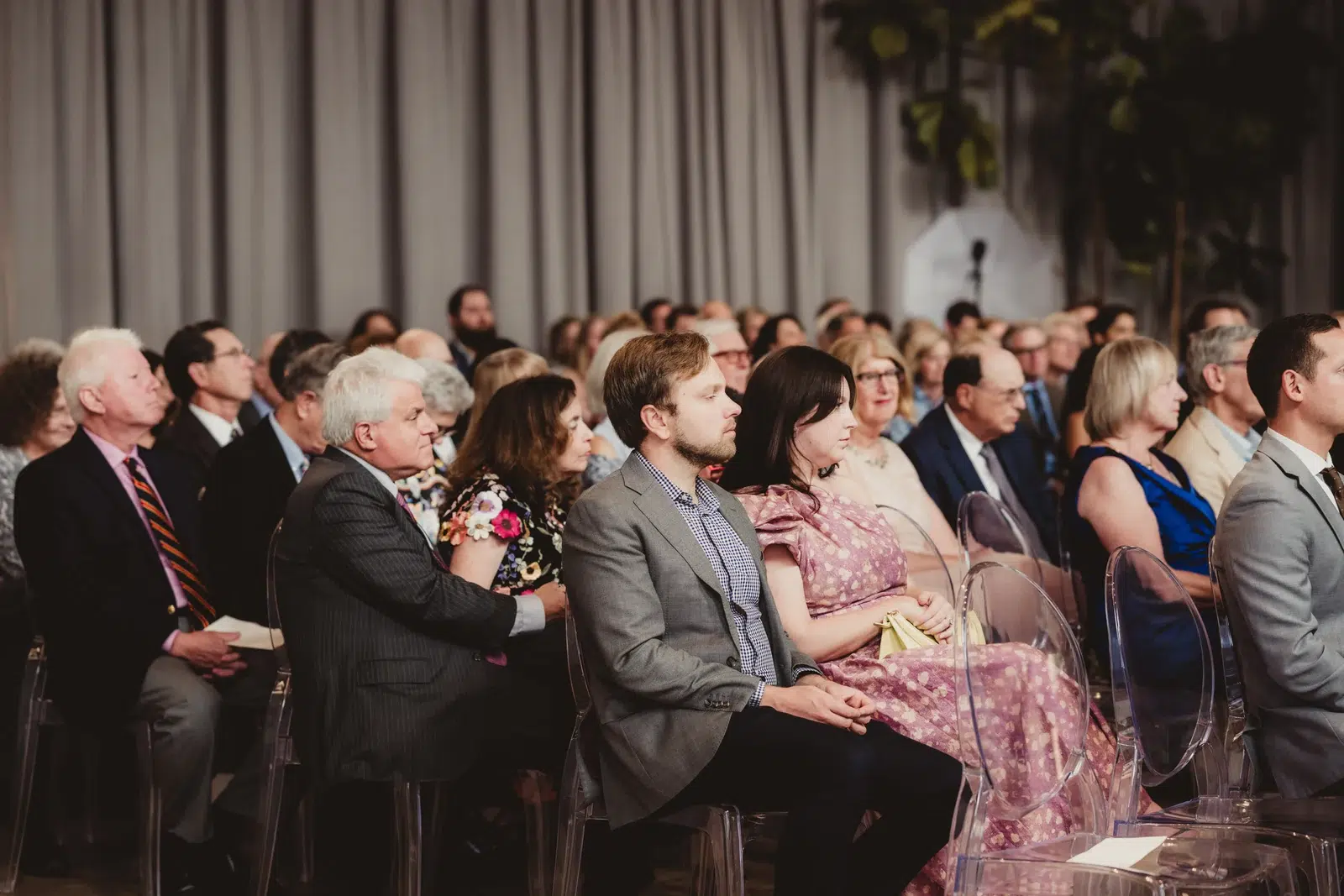 Seated guests watching the ceremony from rows of clear chairs.