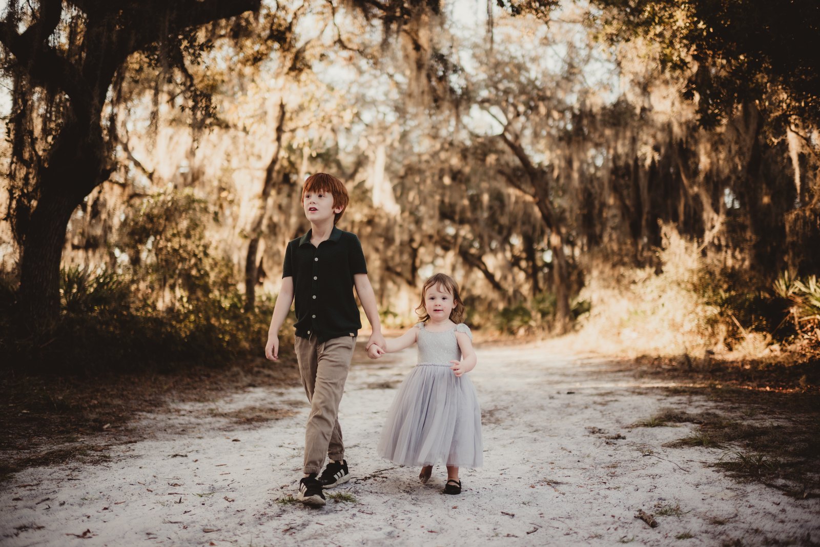 Two children holding hands on a tree-lined sandy path at Aripeka Sandhills Preserve.
