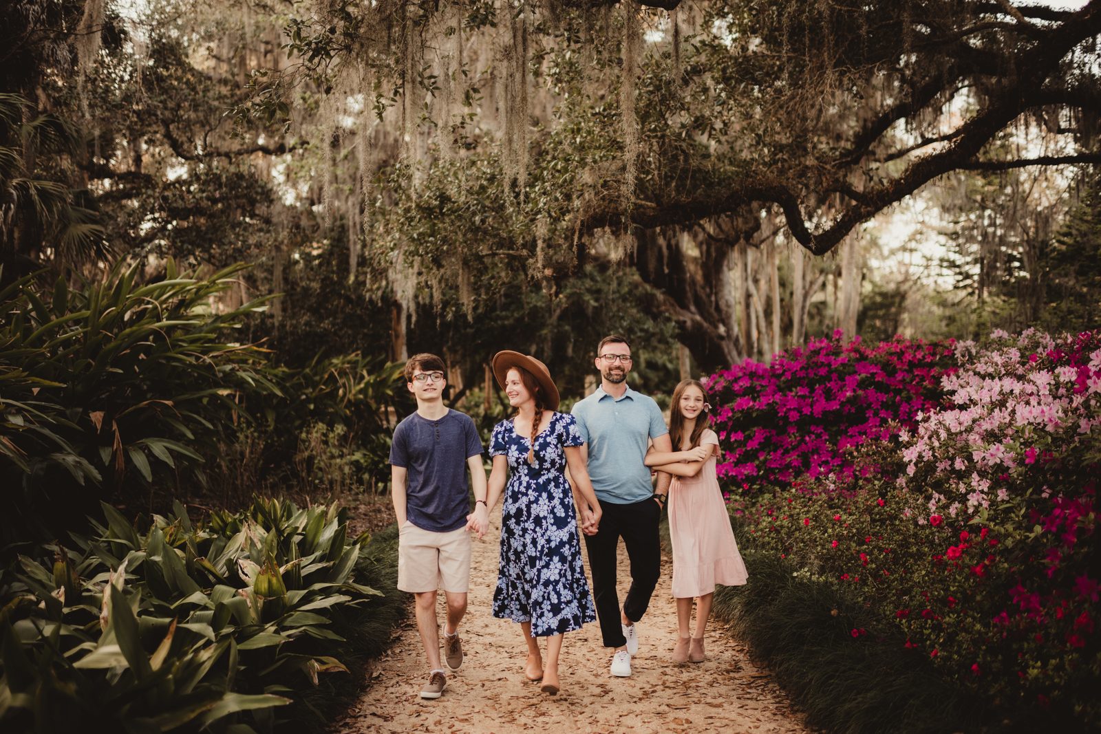 Family walking beneath moss-covered oaks beside flowering shrubs at Washington Oaks Gardens State Park.