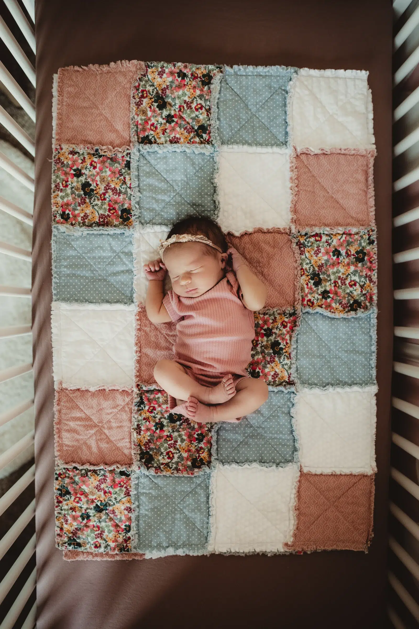Newborn portrait on a patchwork quilt in a crib A newborn resting on a patchwork quilt in a wooden crib.